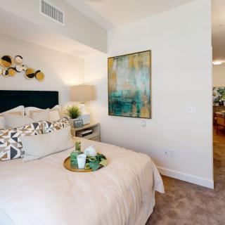 A modern and cozy bedroom featuring stylish decor with artwork on the wall and a neatly arranged bed.