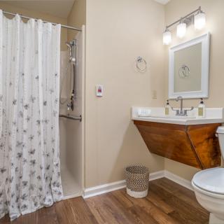 A modern bathroom with a wooden floor, featuring a sleek sink, shower curtain, and contemporary light fixture.