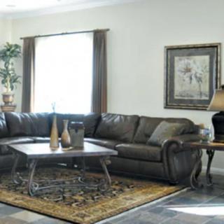 A cozy living room featuring a large leather sectional sofa, a wooden coffee table with decorative items, and a patterned rug. The space is accented with a floor lamp and framed artwork on the wall.