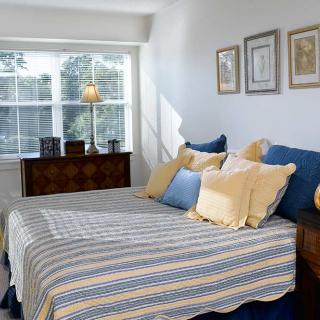 A cozy bedroom with sunlight streaming through a window, featuring a neatly arranged bed with striped bedding and decorative pillows.
