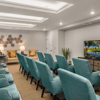 A modern home theater setup with rows of teal chairs facing a large television in a well-lit room.