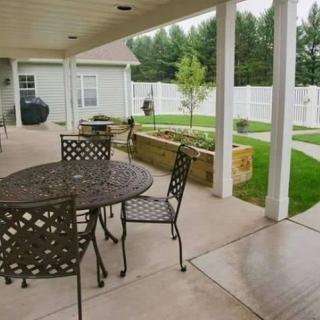 A covered patio with outdoor furniture overlooking a garden and fenced backyard.
