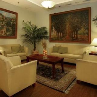 A cozy living room with sofas, armchairs, and a coffee table, adorned with paintings and plants.