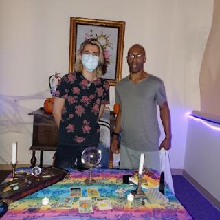 Two individuals standing in a mystical setting with a decorated table.