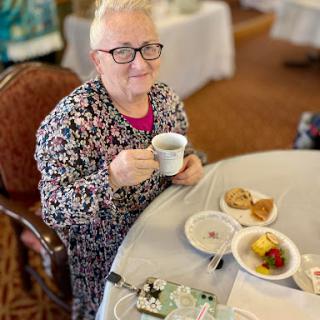 An elderly woman enjoying a cup of tea while seated at a beautifully set table.
