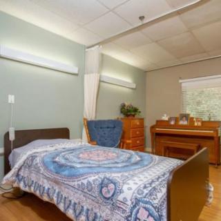 A hospital room with a bed and wooden furniture, featuring a decorative blanket and natural lighting from the window.
