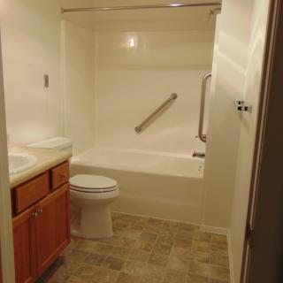 A small bathroom with a bathtub, toilet, sink, and grab bar.