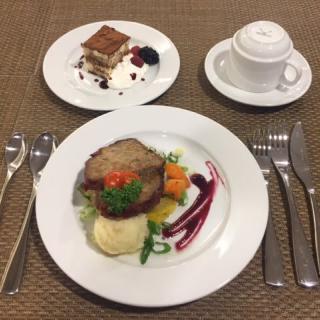 An elegantly plated beef roast with vegetables and potatoes, accompanied by a dessert of tiramisu and a cup of coffee.