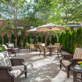 A cozy outdoor patio with chairs, tables, and umbrellas surrounded by lush greenery.