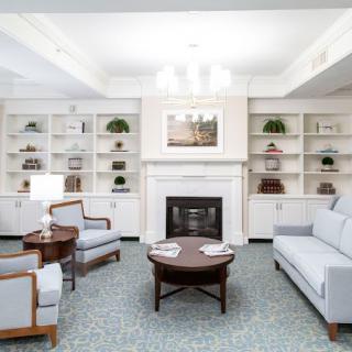 A well-lit living room with a fireplace, surrounded by built-in shelves, sofas, and armchairs.