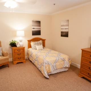 A cozy bedroom featuring a single bed, wooden furniture, and soft lighting complemented by wall art.