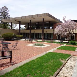 A modern building with a spacious courtyard featuring outdoor seating and blossoming trees.
