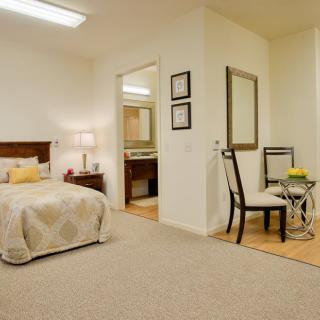 A cozy bedroom with a neatly made bed, a desk area with a chair, and a large mirror.
