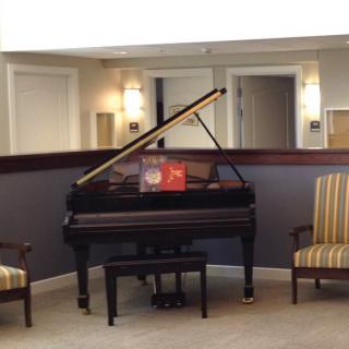 A grand piano with a partially opened lid, flanked by two striped armchairs in a well-lit room.