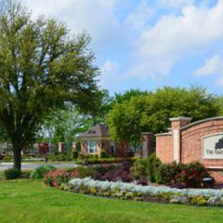 A landscaped suburban entrance with a brick wall and sign surrounded by trees and flowers.