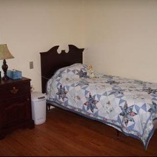 A simple bedroom with a single bed, a nightstand, and a lamp.
