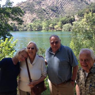 A group of people posing together in front of a lake with trees and hills in the background.