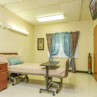 A clean and simple hospital room featuring a single bed, medical equipment, curtains, and a television.