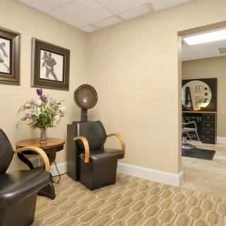 A salon waiting area featuring comfortable chairs, a hairdryer, and decorative artwork.
