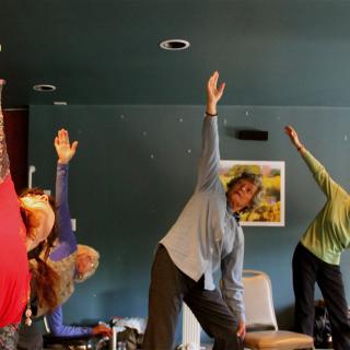 A group of people practicing yoga indoors, performing a stretching exercise together.