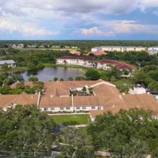 Aerial view of a residential area with buildings surrounded by trees and a lake under a cloudy sky.