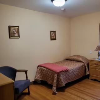 A simple bedroom with a single bed, dresser, and chair.