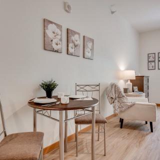 A cozy dining and living area with a small wooden table, two chairs, wall art, and a lamp.