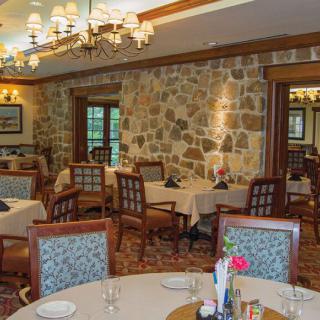 An elegant restaurant dining room featuring stone walls, chandeliers, and neatly set tables.