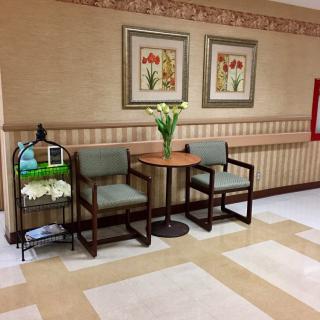 A cozy waiting area with two chairs, a small table with a vase of flowers, and framed artwork on the wall.