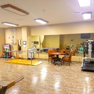 A spacious rehabilitation therapy room equipped with exercise machines and a mirrored wall for monitoring progress.