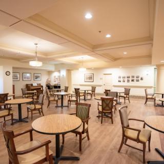 An empty dining room with wooden tables and chairs, featuring warm lighting and decorative wall art.