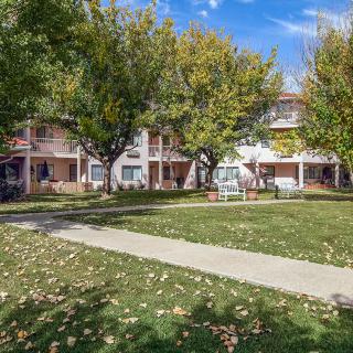 A residential apartment complex surrounded by trees and a well-maintained lawn on a sunny day.