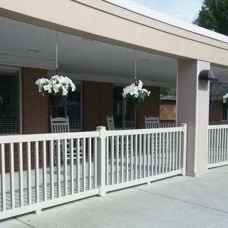 A building patio with white hanging plants and a fenced outdoor seating area.