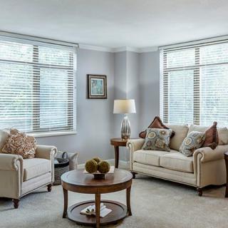 A cozy living room with a sofa, armchair, and coffee table, illuminated by natural light from large windows.