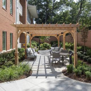 A charming outdoor patio area featuring a wooden pergola with seating and lush landscaping.