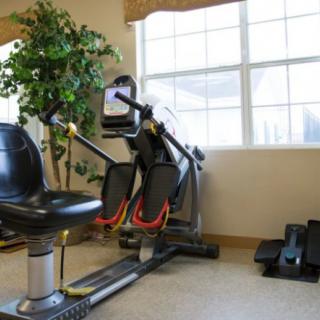 A well-lit room with exercise equipment, including a recumbent bike and elliptical trainer.