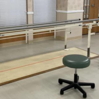 A physical therapy room featuring parallel bars and a stool for rehabilitation exercises.