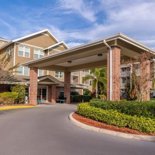 A well-maintained building entrance with a covered driveway and landscaped surroundings under a blue sky.