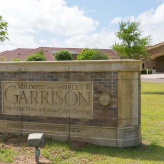 Entrance sign for the building named 'Garrison' with a brick structure and greenery.