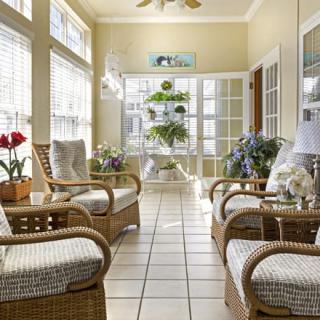 A cozy sunroom featuring rattan furniture and indoor plants, filled with natural light.