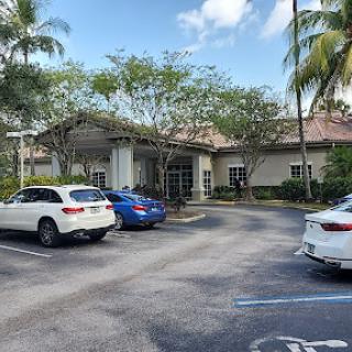 A view of a building surrounded by cars and palm trees under a partly cloudy sky.