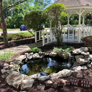 A serene garden scene featuring a pond surrounded by rocks, a wooden gazebo, and a small bridge.