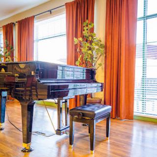 A grand piano elegantly placed in a bright living room, complemented by warm curtains and natural light.