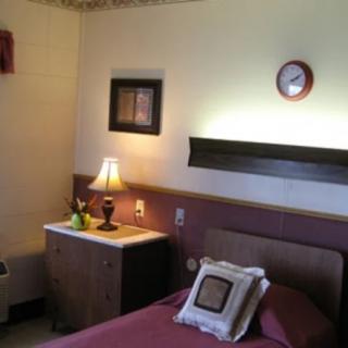 A cozy bedroom featuring a bed with pillows, a side table with a lamp, and wall decorations.