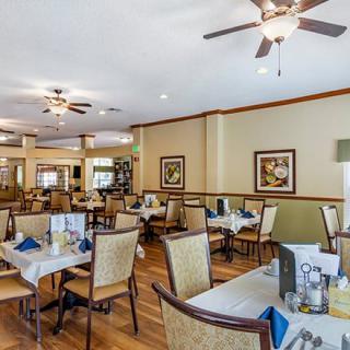 A spacious dining area in a restaurant featuring neatly arranged tables and chairs, warm lighting, and ceiling fans.