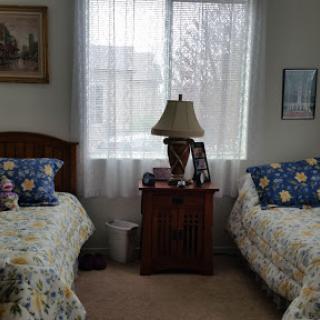 A cozy bedroom featuring two twin beds, a lamp, and bright curtains allowing natural light to fill the space.