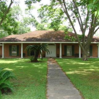 A brick house surrounded by a lush green lawn and trees.