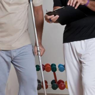 A therapist assists a patient using a crutch during a physical therapy session.