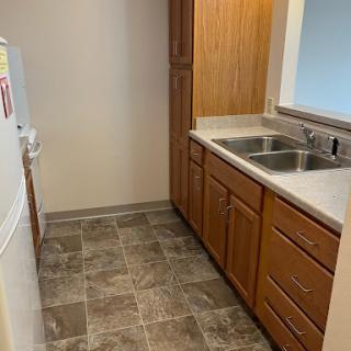 A compact kitchen featuring wooden cabinets, a double sink, and modern flooring.