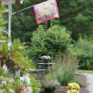 A colorful garden scene with a decorative flag, lush plants, and outdoor seating.